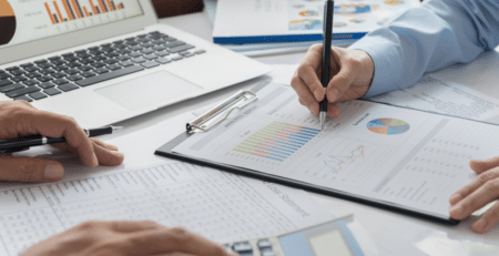 Two peoples hands hovering over accounting & finance documents on a desk with a laptop