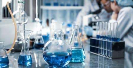 Beakers with blue liquid in a laboratory environment in front of life sciences staff